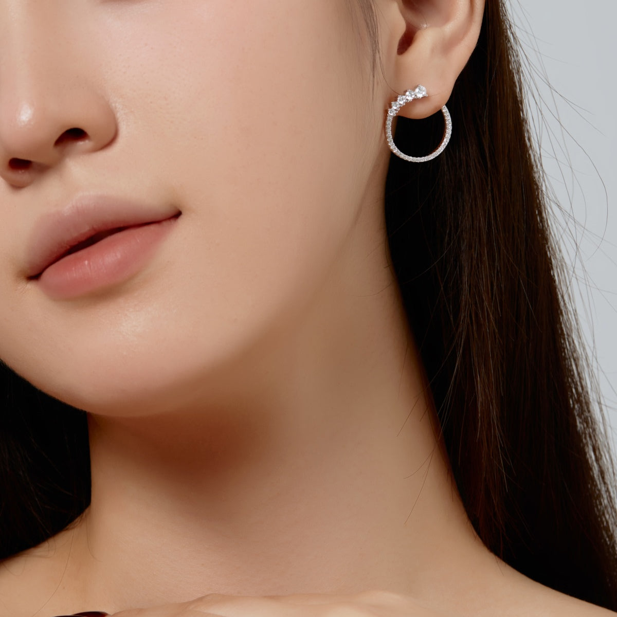 Close-up of a woman wearing silver hoop earrings with a neutral background