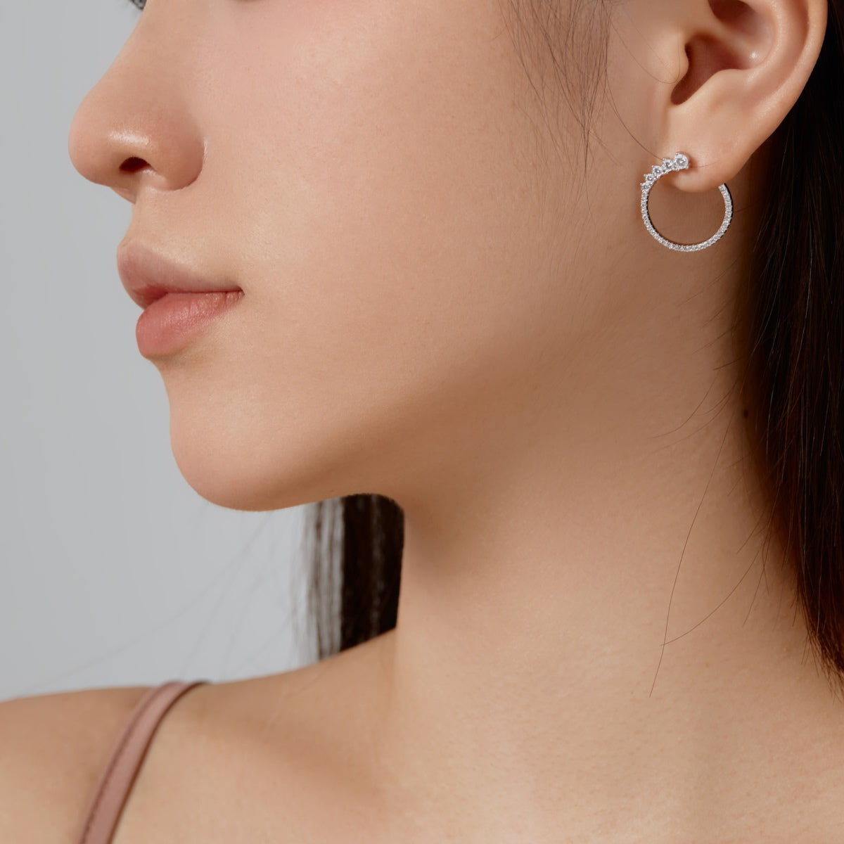 Close-up of a woman wearing a silver hoop earring against a neutral background