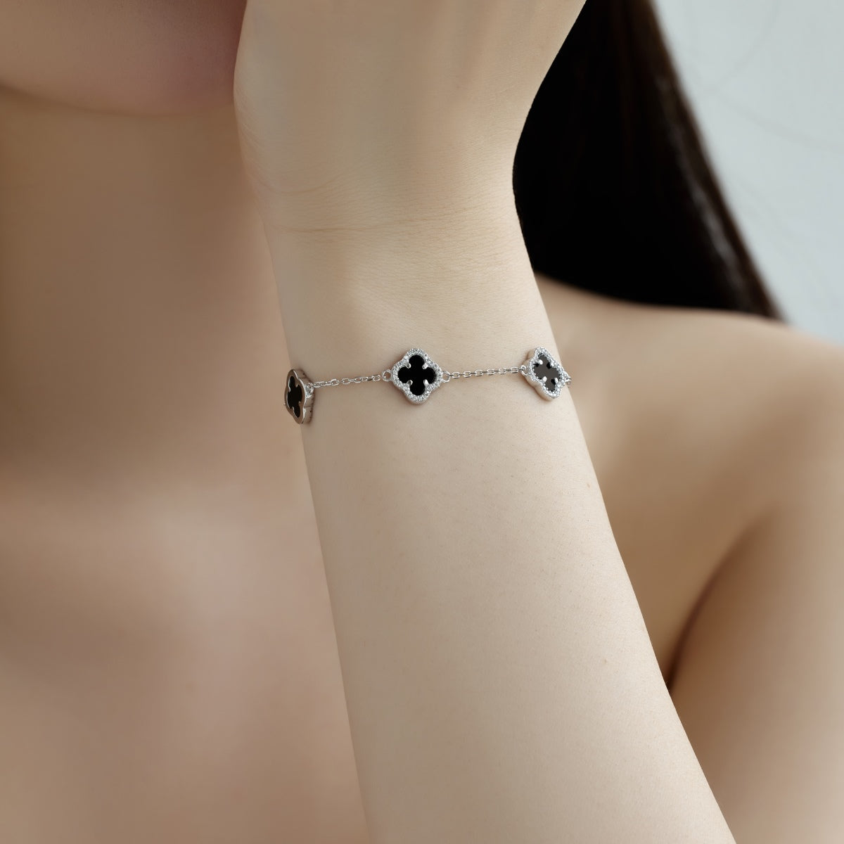 Silver four leaf clover bracelet with black stones on a wrist against a neutral background