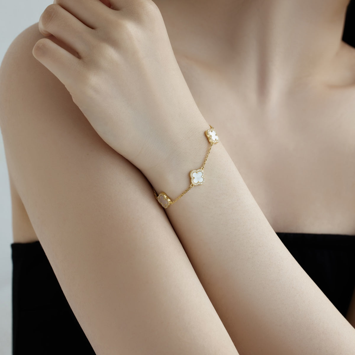 Gold clover bracelet with a four leaf clover motifs on a person's wrist against a neutral background
