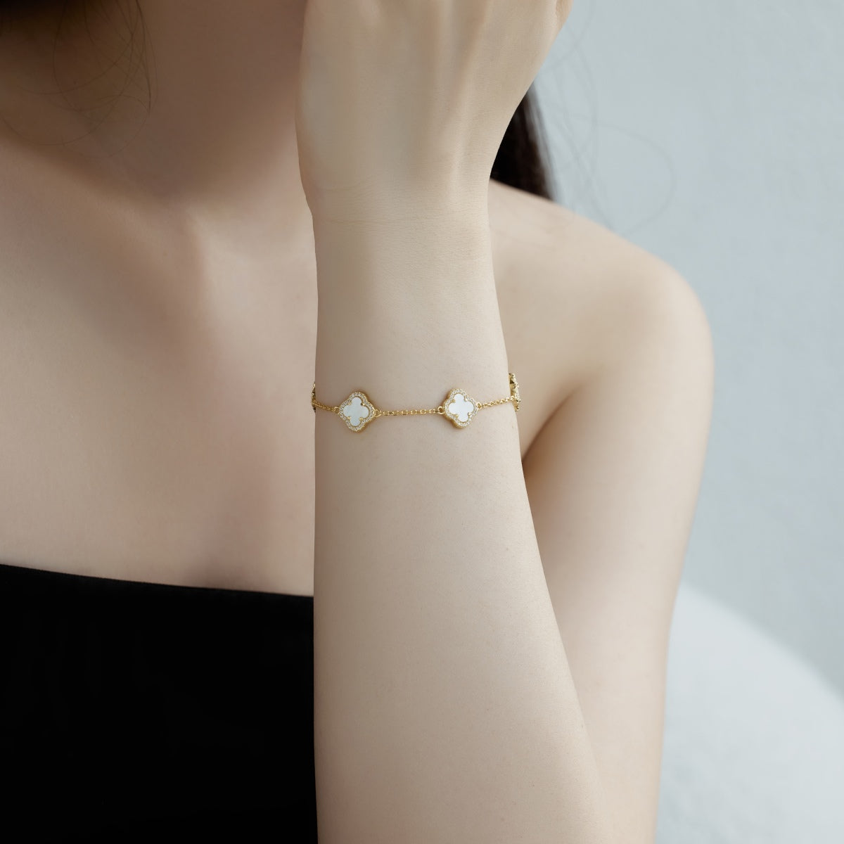 Gold bracelet with four leaf clover  charms on a person's wrist against a neutral background